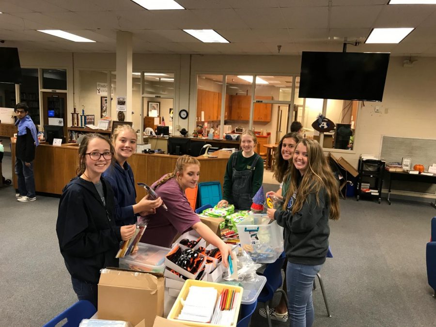 A group of Key Club members stops working for a moment to pose for a photo before resuming putting the bags together. At this table they will pack sun glasses, crayons, and all other manner of fun items into the bag.